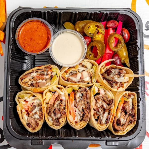 Yalla Shawarma's beef shawarma wraps, with sauces and pickled vegetables, in a black takeout container.