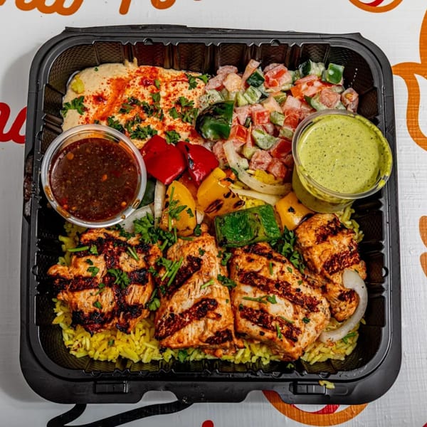 Yalla Shawarma's grilled chicken platter with rice, hummus, salad, and sauces in a black takeout container.