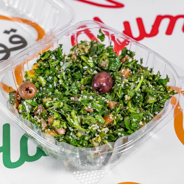 Yalla Shawarma's tabbouleh salad with olives, parsley, tomatoes, and bulgur in a clear plastic container.