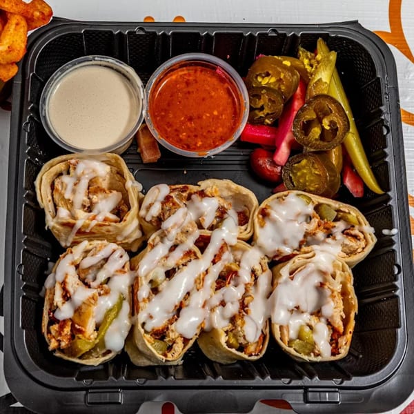 Yalla Shawarma chicken wraps with white sauce, red sauce, and pickled vegetables in a black tray.